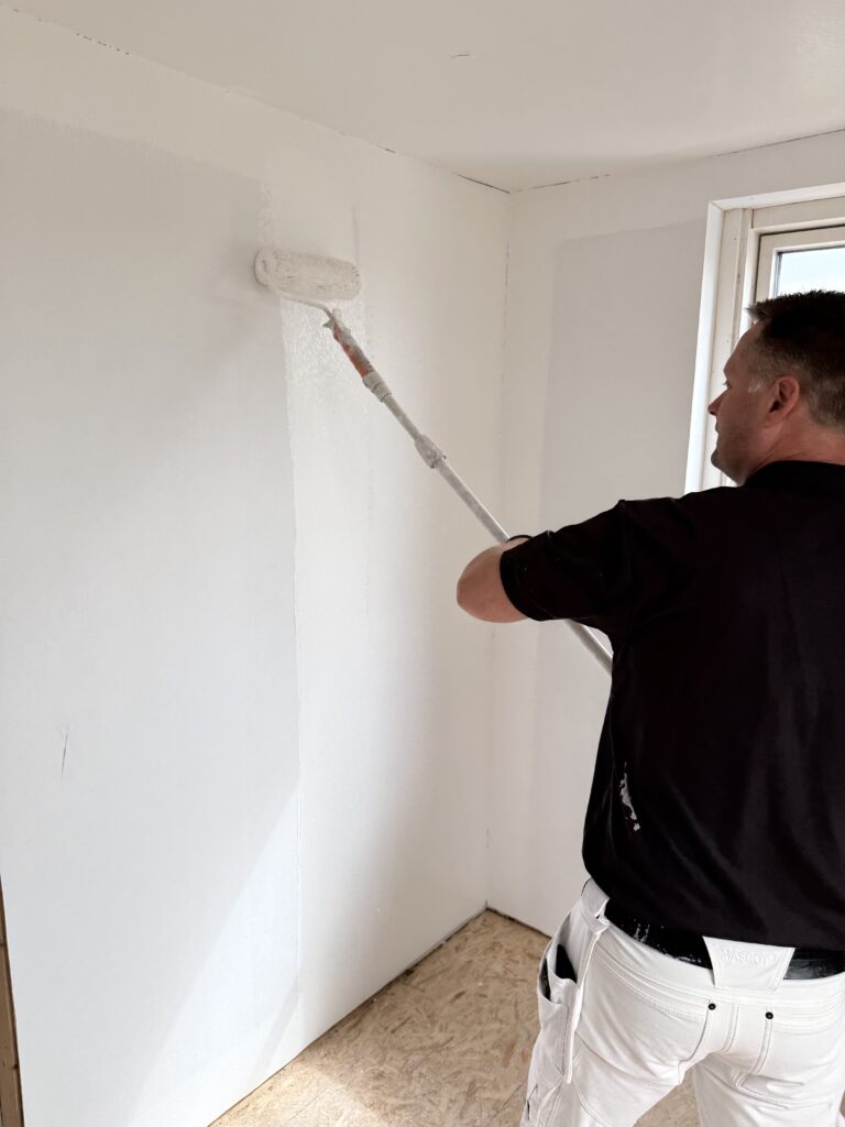 Maler ruller maling på hvid væg